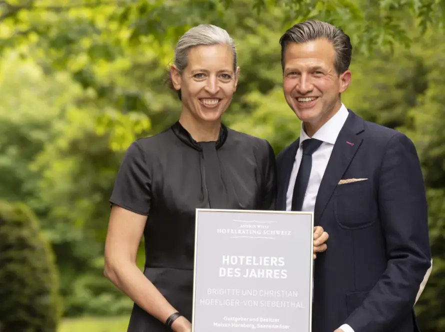 Zwei strahlende Hoteliers mit Auszeichungsurkunde vor grünem Naturhintergrund