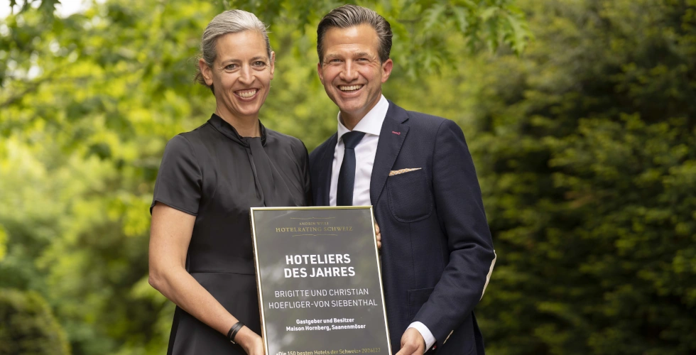 Zwei strahlende Hoteliers mit Auszeichungsurkunde vor grünem Naturhintergrund
